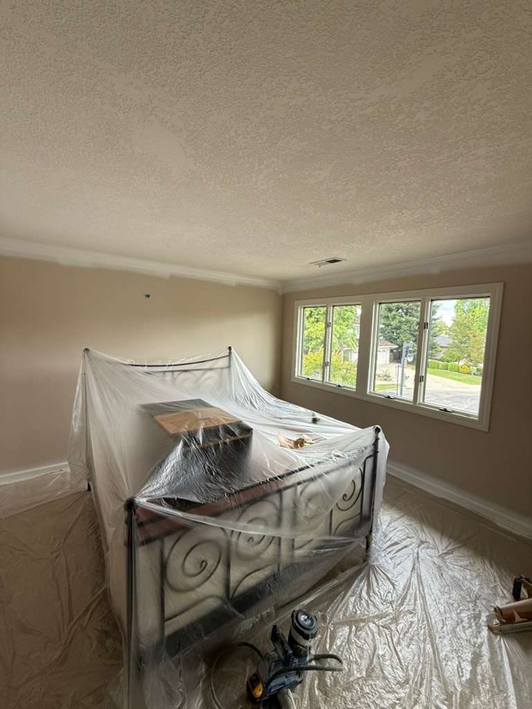 Bedroom fully prepared for residential painting by Alliance Trio Solutions, with furniture wrapped in protective plastic and floors covered with clean drop cloths before painting begins