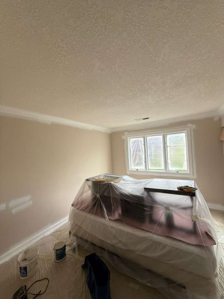 Room mid-project during a professional residential repaint by Alliance Trio Solutions, with furniture wrapped, floors protected, and walls being freshly painted